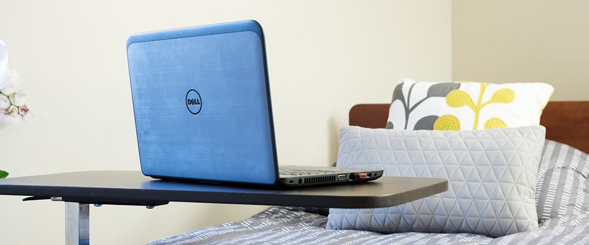 Resident room with laptop on adjustable bed tray and comfortable bedding at Embassy Oaks