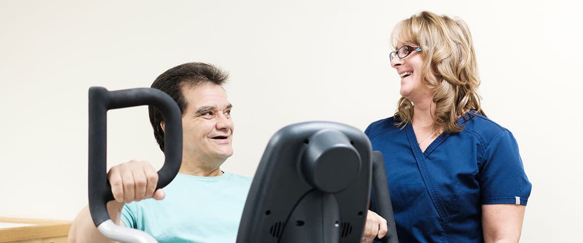 Resident in wheelchair chatting with smiling staff member at Embassy Oaks facility