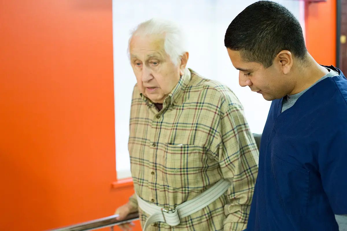 Caregiver supporting an elderly patient through orthopedic recovery exercises