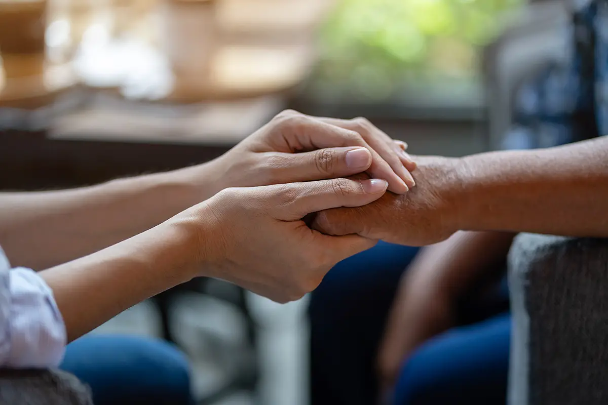 Caregiver holding hands with an elderly person, providing comfort during respite care